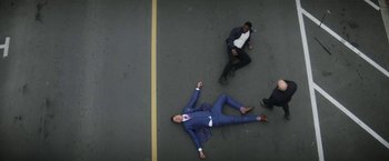 Movie still from “The Man from Toronto” (2022), directed by Patrick Hughes – A man in a blue suit laying on the ground next to another man in a blue suit; Extreme Wide shot, Overhead angle