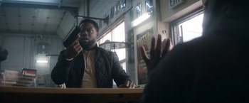 Movie still from “The Man from Toronto” (2022), directed by Patrick Hughes – A man sitting at a table talking on a phone; Medium shot, Over the shoulder angle