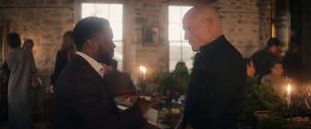 Movie still from “The Man from Toronto” (2022), directed by Patrick Hughes – Two men are shaking hands in front of candles; Medium shot, Over the shoulder angle