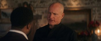 Movie still from “The Man from Toronto” (2022), directed by Patrick Hughes – A man with a bald head is standing in front of a brick wall; Close Up shot, Over the shoulder angle