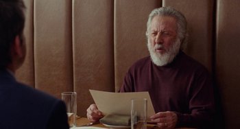 Movie still from “The Meyerowitz Stories” (2017), directed by Noah Baumbach – An older man sitting at a table reading a piece of paper; Close Up shot, Over the shoulder angle
