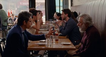 Movie still from “The Meyerowitz Stories” (2017), directed by Noah Baumbach – A group of people sitting at a table with drinks; Medium shot, Over the shoulder angle