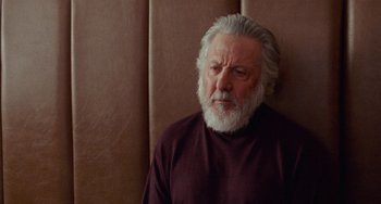Movie still from “The Meyerowitz Stories” (2017), directed by Noah Baumbach – An older man with a beard is sitting against a wall; Close Up shot, Low angle