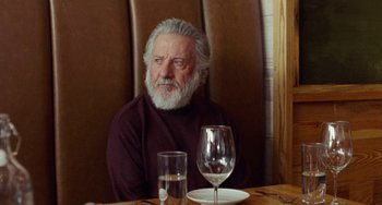 Movie still from “The Meyerowitz Stories” (2017), directed by Noah Baumbach – An older man sitting at a table with a glass of water; Close Up shot, Over the shoulder angle