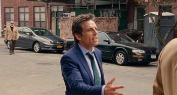 Movie still from “The Meyerowitz Stories” (2017), directed by Noah Baumbach – A man wearing a suit and tie standing on the side of the street; Medium shot, Over the shoulder angle