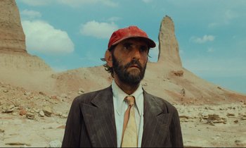Movie still from “Paris, Texas” (1984), directed by Wim Wenders – A man in a suit and a red hat is standing in front of a mountain; Close Up shot, Low angle