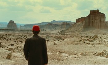 Movie still from “Paris, Texas” (1984), directed by Wim Wenders – A man wearing a red hat standing in the middle of the desert; Extreme Wide shot, Over the shoulder angle
