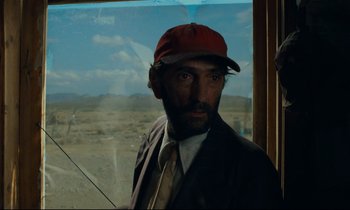 Movie still from “Paris, Texas” (1984), directed by Wim Wenders – A man in a suit and a red hat is standing in front of a window; Close Up shot, Low angle