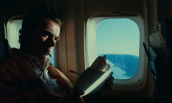 Movie still from “Paris, Texas” (1984), directed by Wim Wenders – A man sitting on a plane looking at a book; Medium shot, Low angle