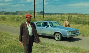 Movie still from “Paris, Texas” (1984), directed by Wim Wenders – A man walking down a road next to a car; Wide shot, Low angle