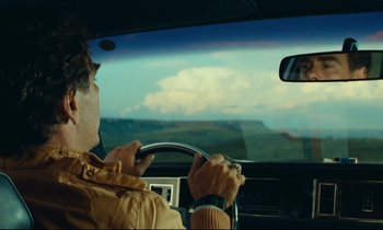 Movie still from “Paris, Texas” (1984), directed by Wim Wenders – A man is driving a car in the day time; Medium shot, Over the shoulder angle