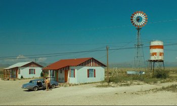Movie still from “Paris, Texas” (1984), directed by Wim Wenders – An old fashioned car parked in front of a house with a windmill in the background; Extreme Wide shot, Low angle