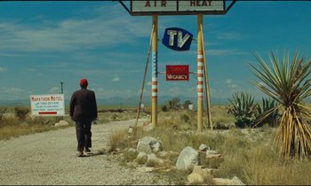 Movie still from “Paris, Texas” (1984), directed by Wim Wenders – A man walking down a dirt road under a sign; Extreme Wide shot, Over the shoulder angle