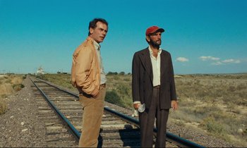 Movie still from “Paris, Texas” (1984), directed by Wim Wenders – Two men standing next to each other on train tracks; Medium shot, Low angle