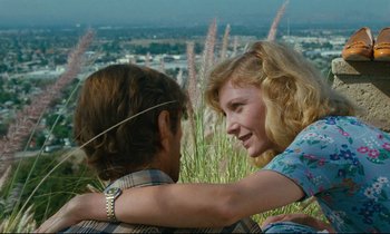 Movie still from “Paris, Texas” (1984), directed by Wim Wenders – A man and a woman sitting in a field of tall grass; Close Up shot, Low angle