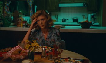 Movie still from “Paris, Texas” (1984), directed by Wim Wenders – A woman sitting at a table with a plate in front of her; Medium shot, High angle