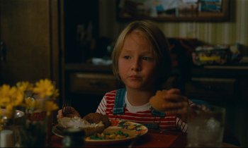 Movie still from “Paris, Texas” (1984), directed by Wim Wenders – A young girl sitting at a table eating a sandwich; Close Up shot, High angle