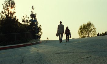 Movie still from “Paris, Texas” (1984), directed by Wim Wenders – A man and a woman walking down a street holding skateboards; Extreme Wide shot, Low angle