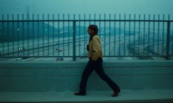 Movie still from “Paris, Texas” (1984), directed by Wim Wenders – A man walking on a sidewalk near a freeway; Wide shot, Low angle