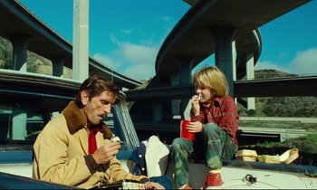 Movie still from “Paris, Texas” (1984), directed by Wim Wenders – A man and a woman sitting next to each other; Medium shot, Low angle