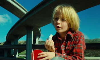 Movie still from “Paris, Texas” (1984), directed by Wim Wenders – A young boy eating a hot dog on a hot dog bun; Medium shot, Low angle