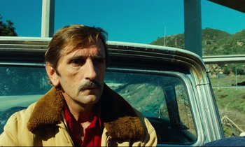 Movie still from “Paris, Texas” (1984), directed by Wim Wenders – A man with a beard and mustache sitting in the back of a car; Close Up shot, Low angle