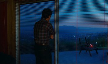 Movie still from “Paris, Texas” (1984), directed by Wim Wenders – A man standing in front of a window looking out at a city; Wide shot, Over the shoulder angle