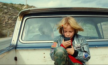 Movie still from “Paris, Texas” (1984), directed by Wim Wenders – A young girl sitting in the back of a car looking at a cell phone; Medium shot, Low angle