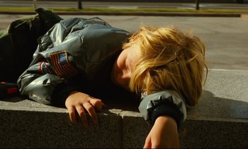 Movie still from “Paris, Texas” (1984), directed by Wim Wenders – A young boy laying on the ground with his head on a wall; Medium shot, High angle