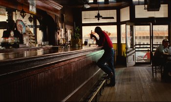 Movie still from “Paris, Texas” (1984), directed by Wim Wenders – A man standing at a bar drinking a beer; Wide shot, Low angle