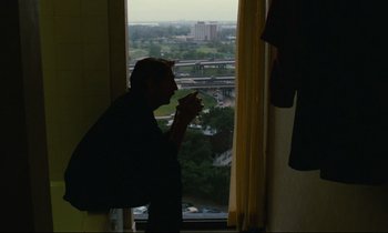 Movie still from “Paris, Texas” (1984), directed by Wim Wenders – A man standing in front of a window taking a picture of a city; Medium shot, Over the shoulder angle