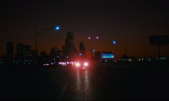 Movie still from “Paris, Texas” (1984), directed by Wim Wenders – A car driving down a street at night with lights on; Extreme Wide shot, High angle