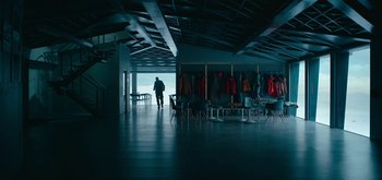 Movie still from “The Midnight Sky” (2020), directed by George Clooney – A man standing in front of a room with a bunch of jackets hanging on the wall; Extreme Wide shot, Low angle