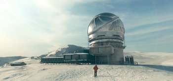 Movie still from “The Midnight Sky” (2020), directed by George Clooney – A person standing in the snow near a large telescope; Extreme Wide shot, Low angle