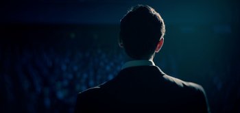 Movie still from “The Midnight Sky” (2020), directed by George Clooney – A man standing in front of an audience at night; Medium shot, Low angle