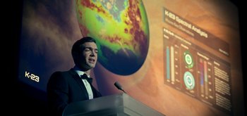 Movie still from “The Midnight Sky” (2020), directed by George Clooney – A man standing at a podium in front of a projection screen; Medium shot, Low angle
