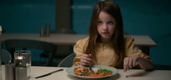 Movie still from “The Midnight Sky” (2020), directed by George Clooney – A little girl sitting at a table with a plate of food in front of her; Close Up shot, High angle