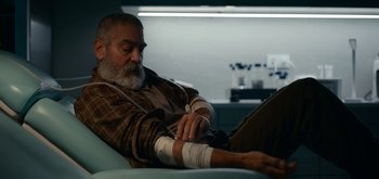 Movie still from “The Midnight Sky” (2020), directed by George Clooney – An older man sitting on a couch with a bandage on his arm; Medium shot, Low angle