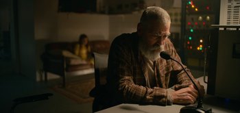 Movie still from “The Midnight Sky” (2020), directed by George Clooney – An older man sitting at a table with a microphone in front of him; Medium shot, Over the shoulder angle