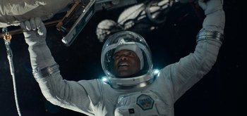 Movie still from “The Midnight Sky” (2020), directed by George Clooney – A man in a spacesuit and a helmet is raising his arms; Medium shot, Overhead angle