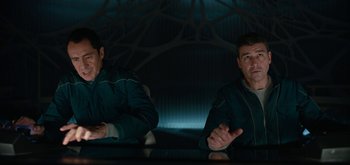 Movie still from “The Midnight Sky” (2020), directed by George Clooney – Two men sitting at a table in a dark room; Medium shot, Over the shoulder angle
