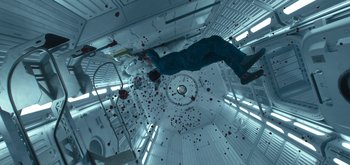Movie still from “The Midnight Sky” (2020), directed by George Clooney – A man is floating in a room with red flowers; Wide shot, Overhead angle