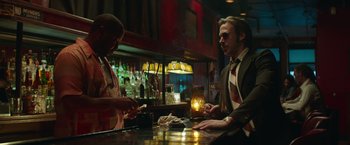 Movie still from “The Nice Guys” (2016), directed by Shane Black – A man sitting at a bar talking to a bartender; Medium shot, Over the shoulder angle