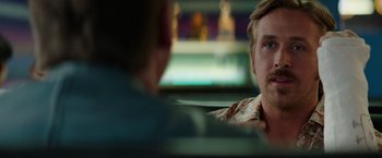 Movie still from “The Nice Guys” (2016), directed by Shane Black – A man sitting in a car with another man in the back seat; Close Up shot, Over the shoulder angle