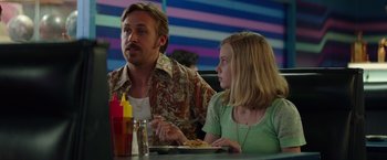 Movie still from “The Nice Guys” (2016), directed by Shane Black – A man and a woman sitting at a table with food; Medium shot, Over the shoulder angle