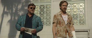Movie still from “The Nice Guys” (2016), directed by Shane Black – Two men standing next to each other holding newspapers; Medium shot, Low angle