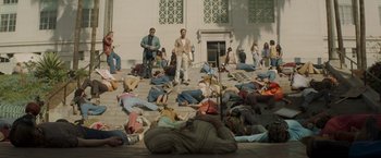 Movie still from “The Nice Guys” (2016), directed by Shane Black – A group of people laying on the steps of a building; Extreme Wide shot, High angle