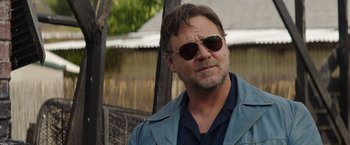 Movie still from “The Nice Guys” (2016), directed by Shane Black – A person wearing sunglasses near a fence; Close Up shot, Over the shoulder angle