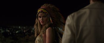 Movie still from “The Nice Guys” (2016), directed by Shane Black – A woman in a native american headdress is posing for a picture; Close Up shot, Over the shoulder angle