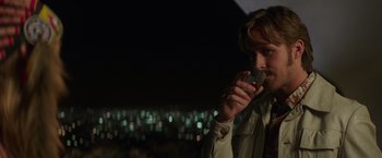 Movie still from “The Nice Guys” (2016), directed by Shane Black – A person holding a cell phone in their hand; Medium shot, Over the shoulder angle